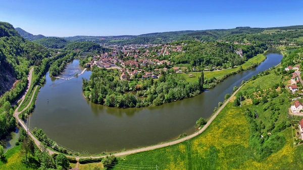 Photographie aérienne ou grand angle du village de Baume-les-Dames dans le Doubs, montrant son identité visuelle distinctive. L'image doit capturer les éléments caractéristiques du village (architecture vernaculaire, présence de la rivière Doubs, environnement naturel et urbain spécifique à Baume-les-Dames), prise de jour avec une excellente luminosité, et offrir une perspective clairement différente des trois autres localités déjà sélectionnées pour couvrir la diversité géographique du département.